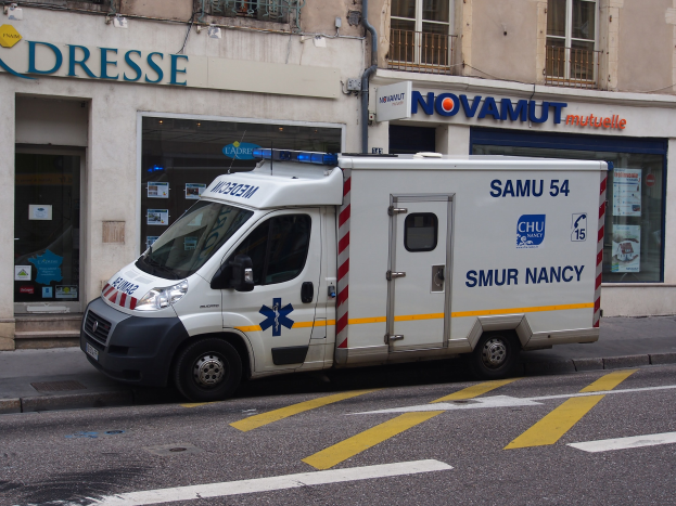 Ambulanz auf dem Seitenstreifen vor einem Krankenhausgebäude mit sichtbarem Text auf Schildern.