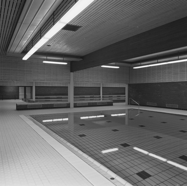 Indoor-Schwimmbad mit klarem Wasser, gefliesten Wänden und Boden, Deckenbeleuchtung und minimalen Umgebungsobjekten in einem großen Gebäude.
