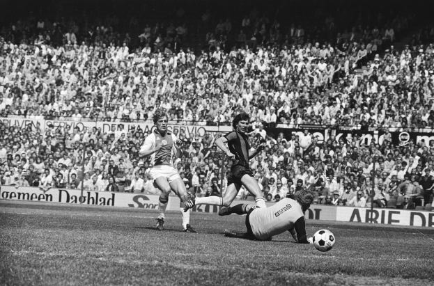 Schwarz-weißes Foto von Männern, die auf einem Feld Füßball spielen, mit Zuschauern im Hintergrund und einem Banner mit der Aufschrift "Bundesliga 1978-79 Ajax 1-1 Hannover 96."