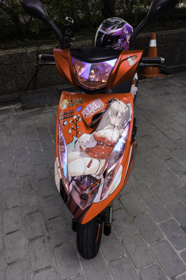 Ein oranges E-Scooter auf einer Straße mit einem Helm daneben, neben einem Verkehrskegel, einer Wand und Bäumen.