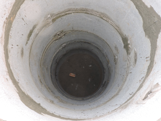 Beton-Abwasserrohr mit mittigem Loch in einer Betonwand, das ein Objekt in seiner Mitte enthält.