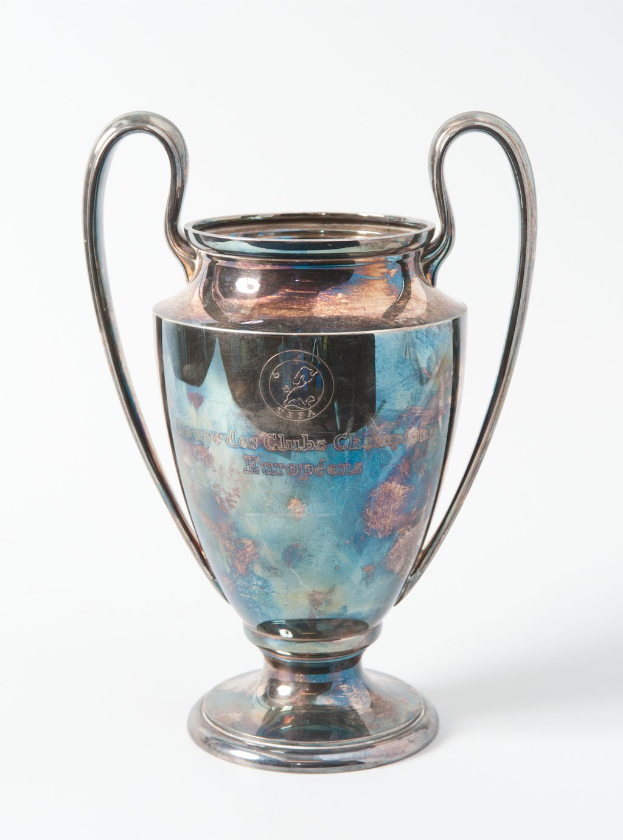 Der UEFA-Champions-League-Pokal, ein stahlerner Pokal mit zwei Griffen und einem blauen und silbernen Farbschema, mit der Inschrift "UEFA Champions League", vor einem weißen Hintergrund.