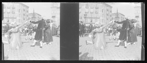 Ein Schwarz-Weiß-Foto einer Gruppe von Menschen, die auf der Straße tanzen und Kostüme tragen, umgeben von Gebäuden, Straßenlaternen und einer klaren Himmel.