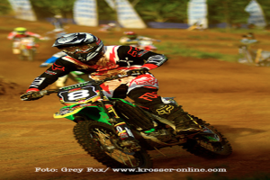 Mehrere Motorradfahrer mit Helmen rasen, mit Text am unteren Bildrand.