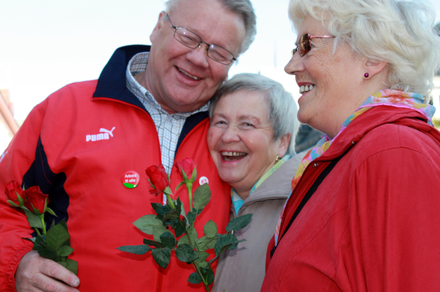 Menschen stehen und lachen in der Mitte des Bildes, umgeben von Rosenblüten mit Blättern.