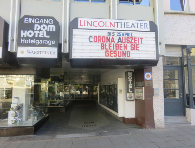 Das Lincoln Theater in Berlin, Deutschland, ein Gebäude mit Glasfenstern und -türen und einer Tafel mit Text darauf, mit verschiedenen Gegenständen im Inneren, die einen belebten Stadtbild Eindruck vermitteln.