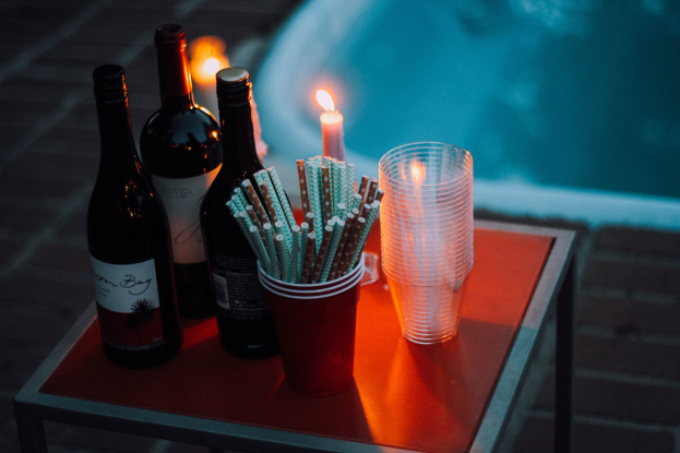 Ein Tisch am Swimmingpool mit zwei Weinflaschen, einer Kerze, Gläsern und Strohhalmen suggeriert Entspannung oder einen Abend auswärts.