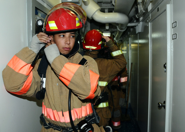 Feuerwehrleute in Uniform in einem Raum mit Rohren und einer Tür während eines Übungsbetriebs.