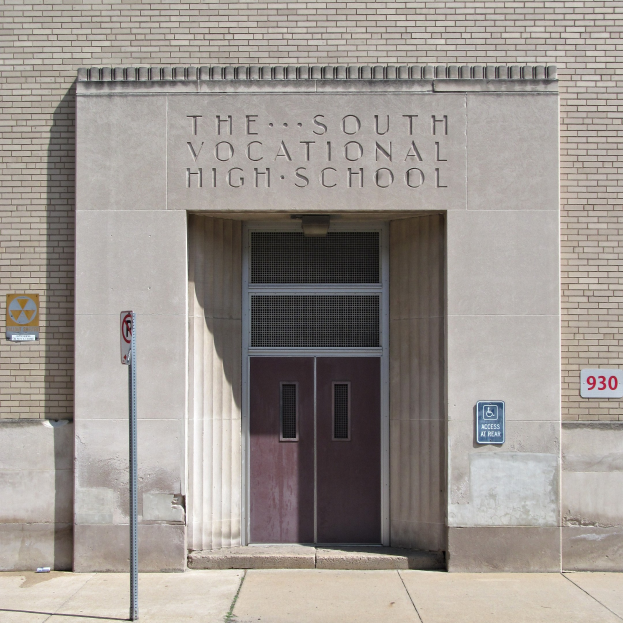 Außenansicht der Südberufsschule mit einer Tür, Schildern und einem Weg, der zur Eingangstür führt.