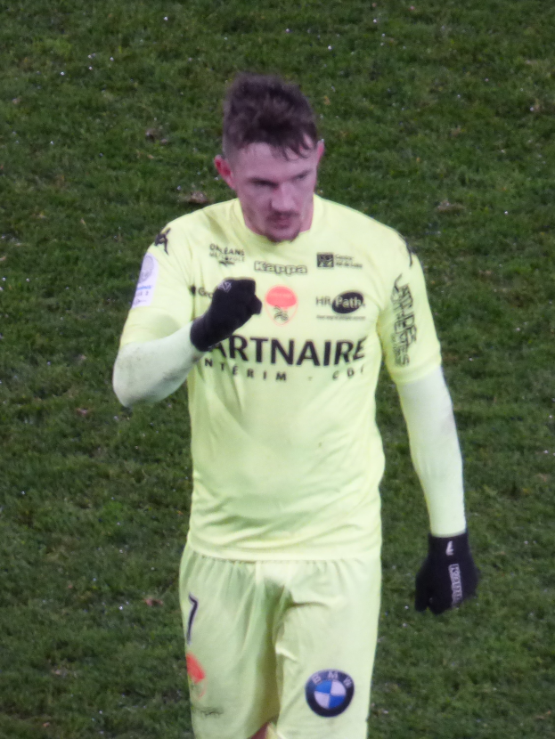 Ein Mann in einem gelben Torwart-Outfit, einschließlich T-Shirt, Shorts und schwarzen Handschuhen, steht auf einem Fußballfeld.