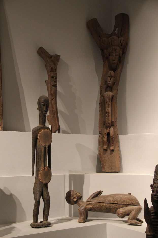 Eine Gruppe von Holzskulpturen auf einer weißen Oberfläche in einem Museum ausgestellt, mit einer Wand im Hintergrund.