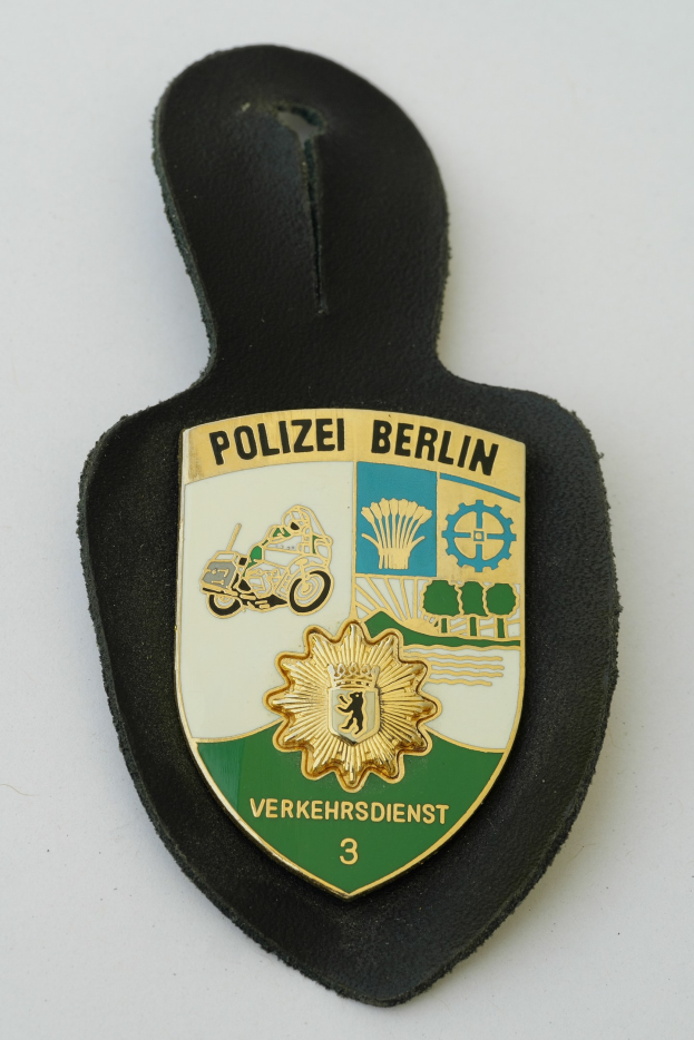 Polizei Berlin Abzeichen mit einem blauen Schild, weißer Grenze, weißer Stern in der Mitte und schwarzer fetter Text auf einer Oberfläche.