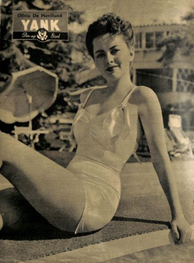 Olivia de Havilland in einem Badeanzug auf dem Boden sitzend und lachend mit Bäumen, Stühlen und einem Gebäude im Hintergrund und Text oben.