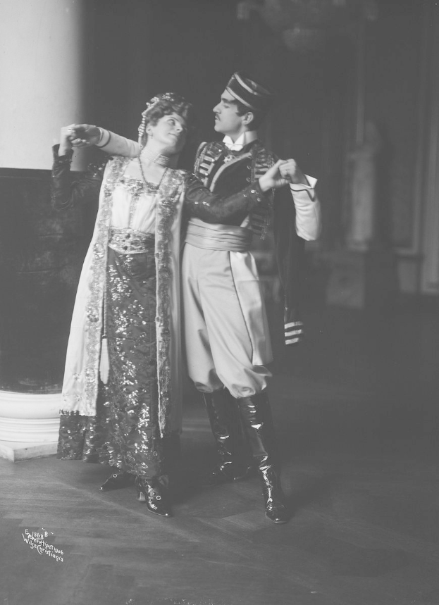 Schwarzes und weißes Foto eines Mannes und einer Frau, die in einem Ballsaal tanzen, mit einer Säule und einer Wand im Hintergrund, der Mann trägt Schuhe während einer Vorstellung.