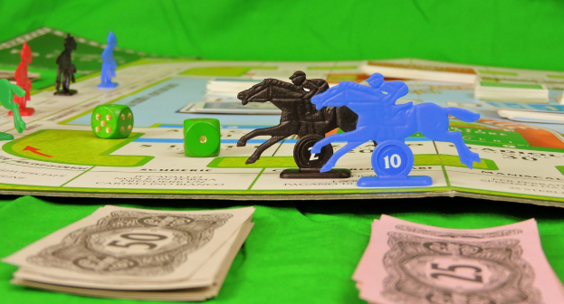 Ein Brettspiel mit einem Pferd- und Reiter-Spielstein, umgeben von Würfeln, Spielzeugen und Münzen auf einem grünen Tuch.