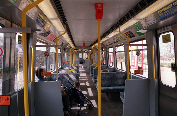 Innensicht eines öffentlichen Verkehrsmittels mit Sitzreihen, einem Kinderwagen und sichtbaren Hinweistafeln.